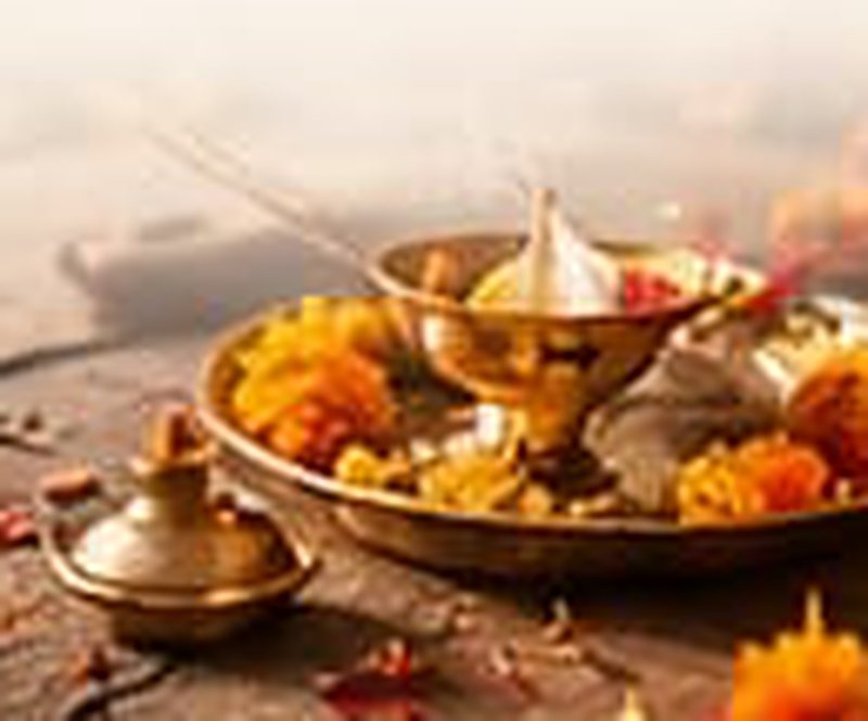 Brass puja thali with a diya, marigold flowers and incense beside the river