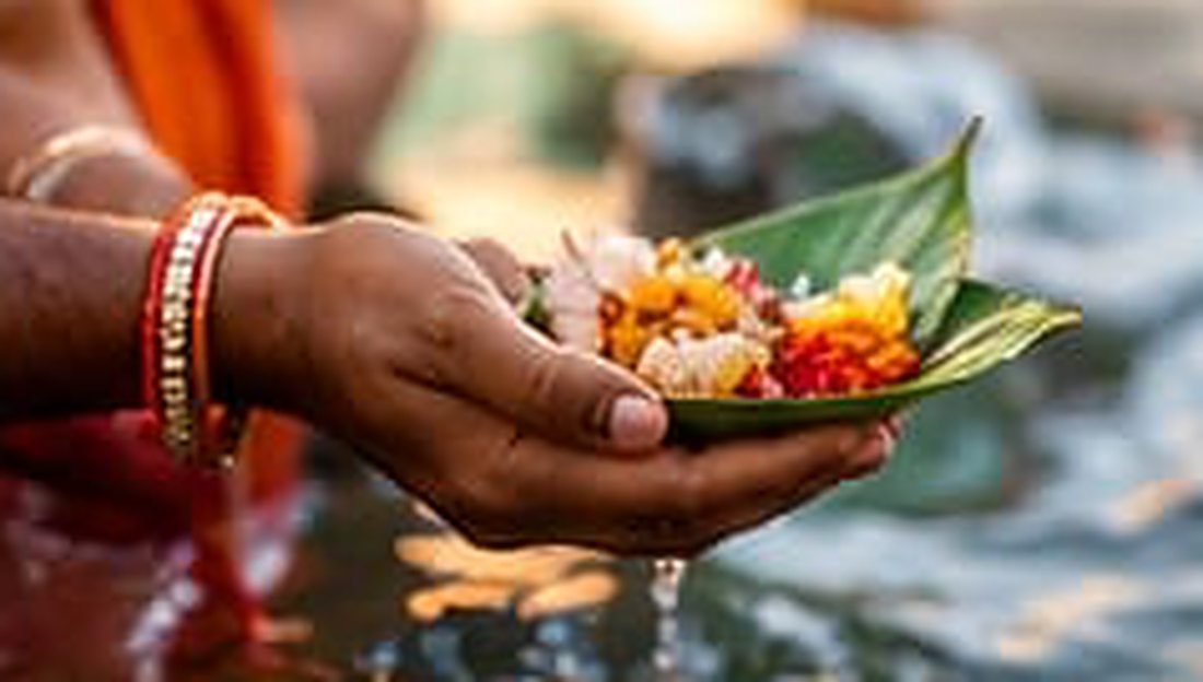 Devotee's hands holding a leaf bowl of flower offerings above the holy river